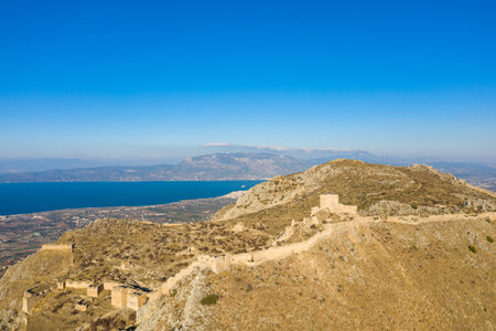 Aerial shot of ancient stone fortifications winding across the sun-bleached slopes of Acrocorinth,...