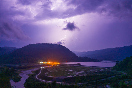 A vivid lightning bolt illuminates dramatic storm clouds above a remote reservoir and terraced...