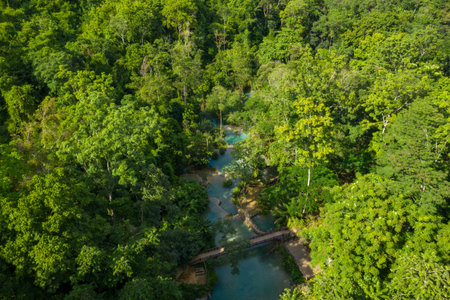 Drone perspective reveals turquoise pools and wooden bridges nestled within dense tropical forest at...