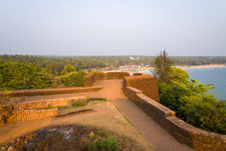 Elevated stone pathway atop historic fort walls offers panoramic views of lush greenery and the sandy coastline at Bekal, India. Soft daylight highlights the textured masonry and tranquil tropical landscape.の写真素材