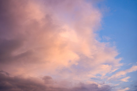 Delicate peach and lavender clouds float across a bright blue sky, creating a serene and airy...