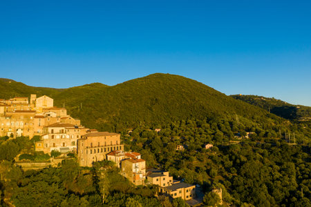Traditional stone buildings of Pisciotta glow in warm evening light, overlooking a lush hillside...