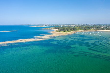 Aerial view of coastal sandbars and geometric oyster beds beneath transparent turquoise water near the shore of Anse de Trehennarvour, Saint Philibert, with boats and a distant village under a sunny sky.の写真素材