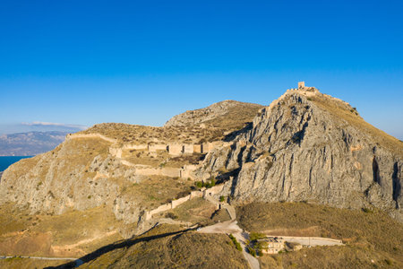 Ancient stone fortifications wind along a rugged hilltop in Acrocorinth, Greece, overlooking...