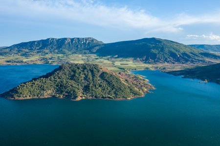 Aerial view of a green, tree-covered peninsula extending into the deep blue waters of Lac de...