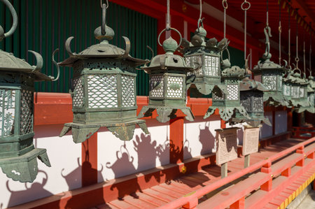 Nara, Japan - November 3, 2023: The image shows a row of bronze lanterns hanging in front of a red and white Kasuga Taisha shrine building with wooden railings and informational signs visible under sunlight.のeditorial素材