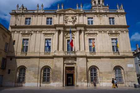 Arles, France - April 1, 2023: The front facade of the Hotel de Ville is shown with multiple flags...