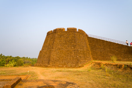 Bekal, India - March 14, 2023: A large corner bastion and adjoining rampart constructed of laterite stone are visible at Bekal Fort, with a dirt path and sparse vegetation in the foreground and a few people walking along the top of the wall.のeditorial素材