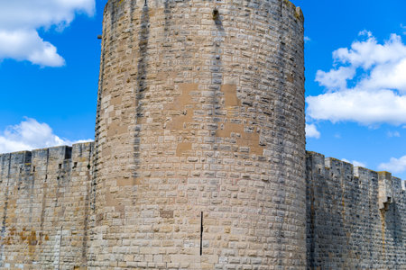 Unknown location - April 2, 2023: The medieval round tower and adjoining stone ramparts of the fortified city of Aigues-Mortes are seen under a blue sky with scattered clouds.のeditorial素材