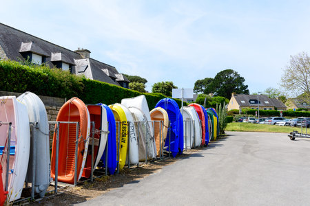Arzon, France - May 29, 2023: Several small rowboats in various colors are stored upright in metal...