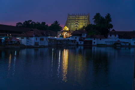 Trivandrum, India - February 28, 2023: The illuminated gopuram of Sree Padmanabhaswamy Temple is visible behind traditional buildings and the sacred temple tank at dusk.のeditorial素材