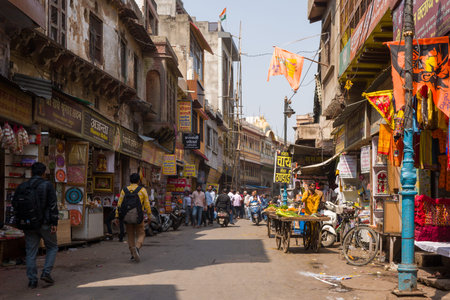 Mathura, India - March 14, 2024: A busy street scene shows pedestrians walking past small shops, market stalls, and street vendors, with signage in Hindi and various goods displayed, in the city center of Mathura.のeditorial素材