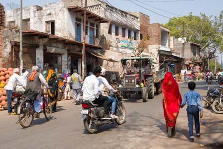 Fatehpur Sikri, India - March 12, 2024: The image shows a lively street scene with people walking, riding bicycles and motorcycles, and a tractor moving past old buildings and market stalls in Fatehpur Sikri.のeditorial素材