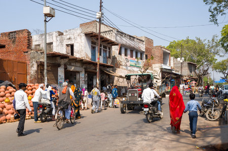 Fatehpur Sikri, India - March 12, 2024: The image shows a busy street with people walking, motorcycles, bicycles, a tractor, and market stalls selling clay pots in front of old buildings in Fatehpur Sikri.のeditorial素材
