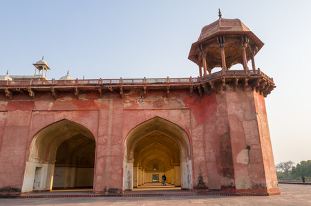 Agra, India - March 12, 2024: The image shows a side view of the red sandstone arcade with arched entrances and an elevated pavilion with chhatri at Akbars Tomb complex under a clear sky.のeditorial素材