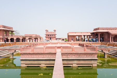 Fatehpur Sikri, India - March 12, 2024: The image shows the central ornamental pool surrounded by red sandstone walkways and pavilions at the Jodha Bai Palace complex, with groups of visitors visible under a clear sky.のeditorial素材