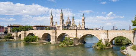 Zaragoza, Spain - May 11, 2024: The image shows the Stone Bridge spanning the Ebro River with the Basilica of Nuestra Senora del Pilar and its towers and domes visible in the background under a partly cloudy sky.のeditorial素材