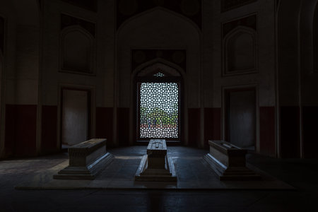 Delhi, India - March 30, 2024: The image shows three marble tombs inside a dimly lit chamber at...