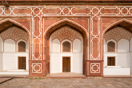 Delhi, India - March 30, 2024: The image shows a section of the arched arcade with red sandstone and white geometric patterns, wooden doors, and decorative lattice windows at Humayuns Tomb.のeditorial素材