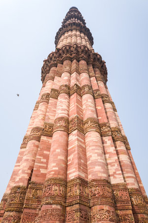 Delhi, India - March 30, 2024: The image shows a low-angle perspective of the Qutub Minar, highlighting its red sandstone surface with ornate stone carvings and Arabic inscriptions under a clear sky.のeditorial素材