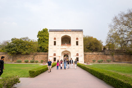 Delhi, India - March 30, 2024: The image shows several people walking along a paved pathway leading to the main entrance gateway of Humayuns Tomb complex, with manicured lawns, hedges, and stone boundary walls visible on both sides.のeditorial素材