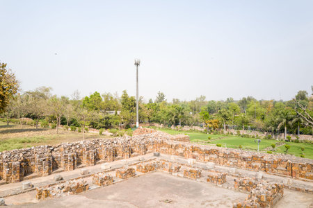 Delhi, India - March 29, 2024: The image shows the weathered stone ruins of Feroz Shah Kotla Fort with landscaped gardens and trees in the background, and a tall communication tower visible beyond the fort walls under a clear sky.のeditorial素材