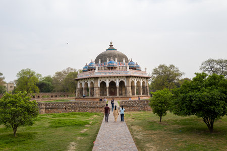 Delhi, India - March 30, 2024: Several people are seen walking along a stone pathway leading to the octagonal Isa Khans Tomb, a domed Mughal-era mausoleum surrounded by gardens and trees within the Humayuns Tomb complex.のeditorial素材
