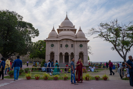 Calcutta, India - March 24, 2024: Groups of people are seen walking, standing, and sitting on the lawn and paved area in front of the Swami Brahmananda Temple at Belur Math, with the domed architecture, potted plants, and trees visible under a partly clouのeditorial素材