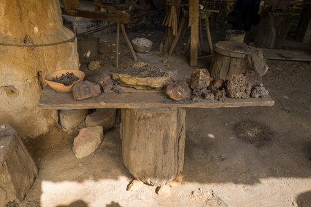 Chateau de Guedelon, France - April 20, 2024: The image shows a rustic wooden table displaying various iron ore rocks, a bowl of metal nails, and stone pieces inside a workshop area at Chateau de Guedelon.のeditorial素材