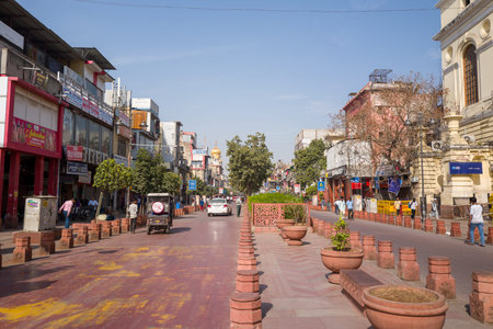 Delhi, India - March 29, 2024: The image shows a wide pedestrianized street lined with commercial buildings, shops, and signage on both sides, with vehicles, pedestrians, large planters, and trees visible under a clear blue sky in Old Delhi.のeditorial素材