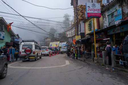 Darjeeling, India - March 27, 2024: Vehicles and pedestrians are visible on a busy street lined with shops and signage, with overhead wires and fog in the background.のeditorial素材