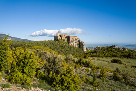 Loarre, Spain - May 7, 2024: Wide view of Loarre Castle situated on a rocky outcrop above a dense forest, with open countryside and a clear blue sky in the background.のeditorial素材