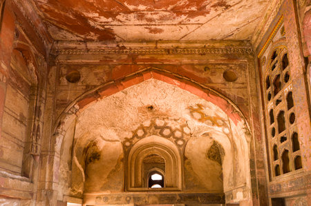 Agra, India - March 11, 2024: The image shows a damaged arched ceiling and wall with faded plaster, exposed brickwork, and geometric patterns at Jahangir Palace in Agra Fort, with part of a decorative window visible on the right.のeditorial素材
