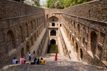Delhi, India - March 29, 2024: People are seen sitting and walking on the stone steps of Agrasen ki Baoli, a historic stepwell with arched niches and deep central well, under daylight.のeditorial素材