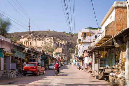 Bundi, India - March 19, 2022: A street in Bundi features shops, parked vehicles, overhead wires, and a distant view of Garh Palace on a hillside during daylight.のeditorial素材