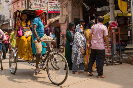Varanasi, India - March 18, 2024: A rickshaw puller pedals a cycle rickshaw carrying a woman in a...