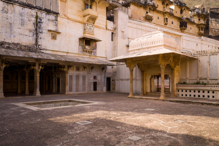 Bundi, India - March 20, 2022: The image shows an inner courtyard at Garh Palace featuring a covered pavilion with carved stone columns, a rectangular stepwell, and multi-level palace buildings with decorative lattice walls.のeditorial素材