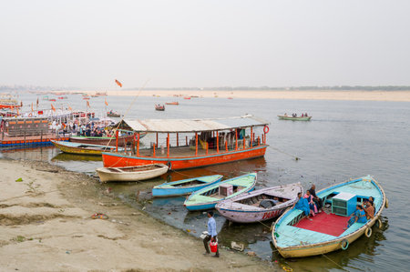 Varanasi, India - March 18, 2024: Several colorful boats are moored along the riverbank at Maharaja Harishchandra Ghat, with groups of people sitting and standing on the boats and along the shore of the Ganges River.のeditorial素材