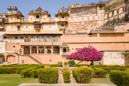 Bundi, India - March 20, 2022: The image shows a flowering tree with bright pink blossoms, a marble bench, manicured hedges, and the historic exterior of Garh Palace under a clear sky.のeditorial素材