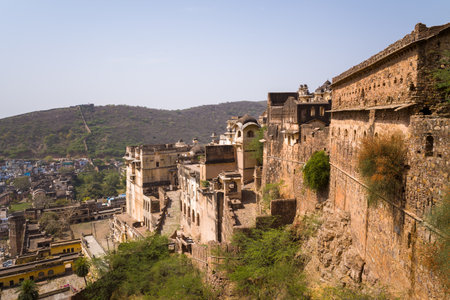 Garh Palace, India - March 20, 2022: Sections of Garh Palace are visible with weathered stone and plaster walls, arched windows, and defensive ramparts set against a dry hillside under a clear sky.のeditorial素材