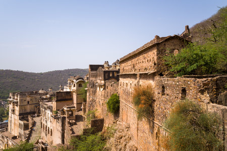 Garh Palace, India - March 20, 2022: Sections of Garh Palace are visible with weathered stone and plaster walls, arched windows, and defensive ramparts set against a dry hillside under a clear sky.のeditorial素材
