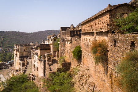 Garh Palace, India - March 20, 2022: The exterior of Garh Palace is shown with weathered stone and plaster buildings, arched windows, balconies, and defensive walls set on a hillside under a clear sky.のeditorial素材