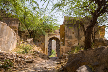 Taragarh Fort, India - March 20, 2022: The image shows a stone pathway leading to an arched entrance gate at Taragarh Fort, with weathered walls, scattered rocks, and trees providing partial shade.のeditorial素材