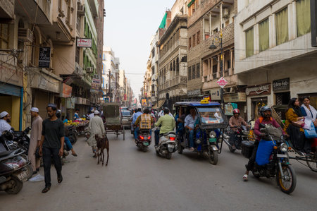 Varanasi, India - March 18, 2024: Pedestrians, motorcycles, auto rickshaws, a goat, and street vendors are visible on a busy urban street lined with multi-story buildings, shops, and signage in Varanasi.のeditorial素材