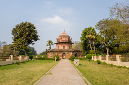 Prayagraj, India - March 21, 2024: The image shows the front view of the tomb of Bibi Tamolon at Khusro Bagh, a Mughal-era sandstone mausoleum with a central dome, surrounded by manicured lawns, trees, and a paved walkway during daylight.のeditorial素材