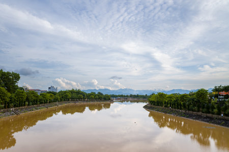 Dien Bien Phu, Vietnam - September 4, 2022: The Nam Rom River is shown with muddy water reflecting the sky, flanked by tree-lined embankments and distant mountains under a partly cloudy sky.のeditorial素材