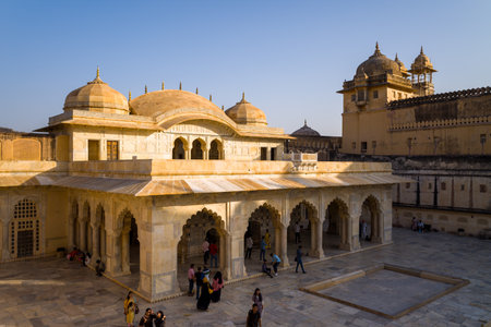 Amber, India - March 16, 2022: The image shows the Sheesh Mahal pavilion with its domed roof, arched colonnade, and open courtyard at Fort dAmber, with several people visible and yellow stone architecture under a clear sky.のeditorial素材