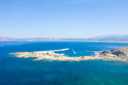 Kissamos, Greece - October 23, 2022: Aerial view of the Port of Kissamos with ferries docked at the piers, breakwaters extending into the sea, and surrounding rocky coastline under a clear sky.のeditorial素材