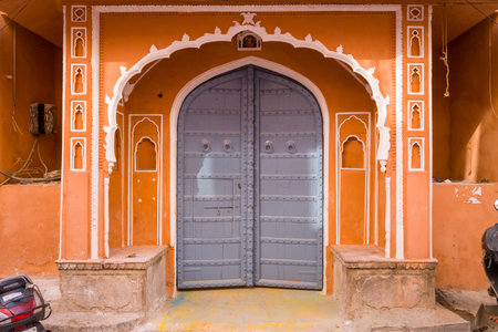 Jaipur, India - March 15, 2022: Ornate arched doorway with a large grey metal door set in an orange wall with white decorative trim and architectural details in the old city.のeditorial素材