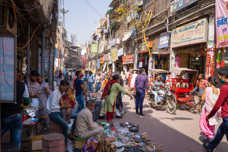 Delhi, India - March 13, 2022: Street vendors sell kitchenware and goods along a crowded market street with pedestrians, shoppers, and cycle rickshaws, with commercial signage and multi-story buildings visible in Old Delhi.のeditorial素材